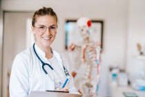 Portrait of smiling female doctor with anatomical skeleton in the background — Stock Photo