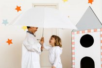 Siblings playing astronaut and researcher with umbrella at rocket — Stock Photo