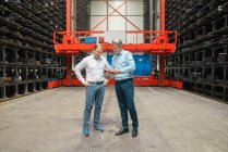 Deux hommes d'affaires avec tablette dans un entrepôt haut rack d'une usine — Photo de stock