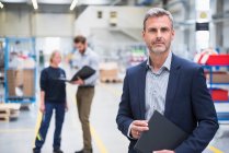 Portrait of a confident mature businessman in a factory with colleagues in background — Stock Photo