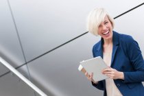 Retrato de mujer de negocios rubia riendo con tableta y café para llevar - foto de stock