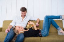 Sorridente donna mangiare croissant mentre sdraiato sulle ginocchia del fidanzato a casa — Foto stock