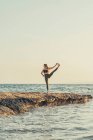 Femme mûre pratiquant le yoga à la plage de rochers le soir — Photo de stock