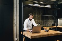 Mature businessman working in kitchen, using laptop — Stock Photo