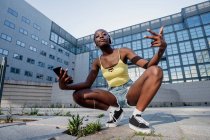 Young woman listening music through headphones crouching on footpath against building in city — Photo de stock