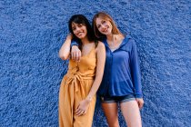 Smiling female friends standing against blue wall in city — Stock Photo