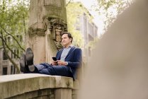 Uomo d'affari maturo con smartphone seduto su una balaustra ponte — Foto stock