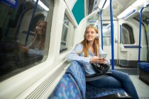 Schöne junge Frau, die durch Fenster schaut, während sie im Zug Musik hört — Stockfoto