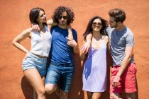 Happy young male and female multi-ethnic friends standing against brown wall on sunny day — Stock Photo