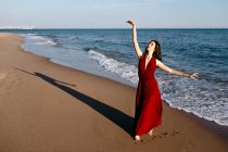 Delicate woman in red dress dancing at the sea, feeling the sun — Photo de stock