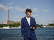 Profesional masculino usando teléfono móvil mientras está parado contra el río Rin durante el día soleado - foto de stock