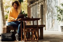 Весела молода жінка, дивлячись далеко, сидячи з цифровим планшетом на тротуарному кафе в місті — стокове фото