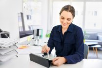 Smiling creative businesswoman using digital tablet at desk in office — Stock Photo