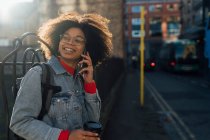 Afro mujer joven hablando por teléfono móvil mientras está de pie en la calle en la ciudad - foto de stock