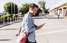 Lächelnder junger Mann benutzt Handy beim Gehen auf der Straße in der Stadt — Stockfoto