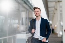 Smiling businessman with newspaper and bag walking in city — Stock Photo