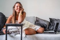 Улыбающаяся женщина со смартфоном сидит дома на диване — стоковое фото