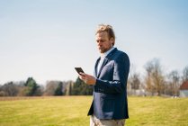 Empresario usando teléfono inteligente mientras está de pie en el parque contra el cielo despejado en el día soleado - foto de stock