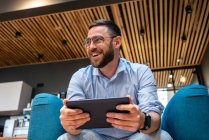 Счастливый мужчина предприниматель смотрит в сторону во время видеозвонка через цифровой планшет в офисной столовой — стоковое фото