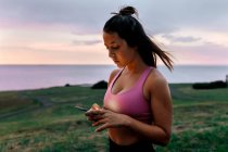 Young sportswoman using smart phone while standing against sky during sunset — Stock Photo
