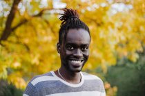 Giovane sorridente in piedi contro albero giallo nel parco durante l'autunno — Foto stock