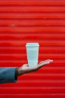 Чоловік тримає одноразову чашу в руці проти червоної стіни. — стокове фото
