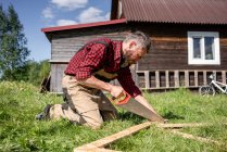 Carpenter working with hand saw cutting plank for playhouse on sunny day — Foto stock