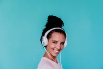 Улыбающаяся красивая женщина слушает музыку через наушники на бирюзовом фоне — стоковое фото