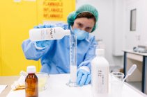 Farmacista femminile versando chimica in cilindro graduato sul tavolo in laboratorio — Foto stock