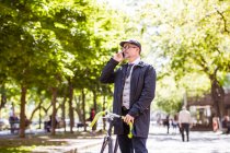 Hombre de negocios maduro con bicicleta y smartphone en la ciudad - foto de stock