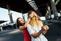 Mujer joven cubriendo los ojos del novio hipster por detrás, mientras que de pie en la calle en la ciudad - foto de stock