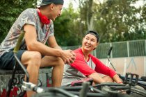 Sorrindo jovens motociclistas BMX masculinos sentados no parque de skate — Fotografia de Stock