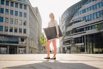 Sonriente hermosa empresaria sosteniendo el panel solar mientras está de pie en el sendero en el distrito financiero - foto de stock