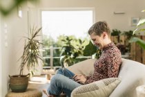 Smiling woman using laptop while sitting on sofa in living room at home — Stock Photo