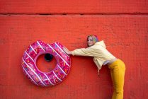 Young woman with dyed hair and floating tyre hanging on red wall — Photo de stock
