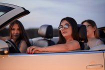 Amigos femininos sentados no conversível contra o céu ao entardecer — Fotografia de Stock