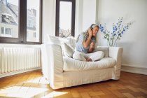 Happy woman listening to music on sofa at home — Stock Photo