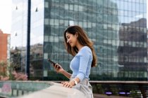 Smiling young businesswoman using smart phone while standing on footbridge — Stock Photo
