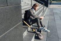 Мужчина пригородный с помощью цифрового планшета, сидя с электрическим самокатом на ступеньках в центре города — стоковое фото