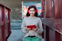 Улыбающаяся красивая женщина слушает музыку в наушниках, держа в руках цифровой планшет — стоковое фото
