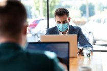 Businessman wearing protective face mask while using laptop in cafe during coronavirus outbreak — Stock Photo