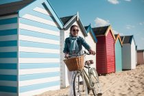 Frau läuft an sonnigem Tag mit Fahrrad auf Sand bei Strandhütten — Stockfoto