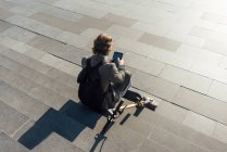 Молодой предприниматель, используя цифровой планшет, сидя с электрическим самокатом на ступенях в центре города в солнечный день — стоковое фото