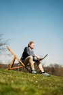 Superficie vista livello di imprenditore maschio guardando lontano mentre seduto con computer portatile sulla sedia a parco durante la soleggiata giornata estiva — Foto stock