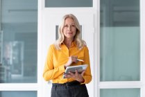 Confident female entrepreneur holding digital tablet while standing against wall in home office — Stock Photo