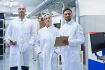 Científicos hombres y mujeres confiados de pie en bata de laboratorio blanca en laboratorio iluminado - foto de stock