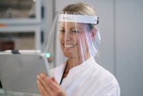 Щаслива жінка-науковець у захисному щиті під час використання цифрового планшета в лабораторії. — стокове фото