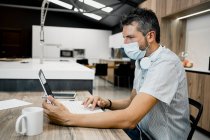 Businessman wearing protective mask while using laptop at desk in office during COVID-19 pandemic — Stock Photo