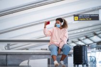 Young woman taking selfie while listening music through headphone at airport — Stock Photo