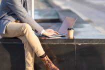 Empresario con taza de café usando portátil mientras está sentado en el banco - foto de stock